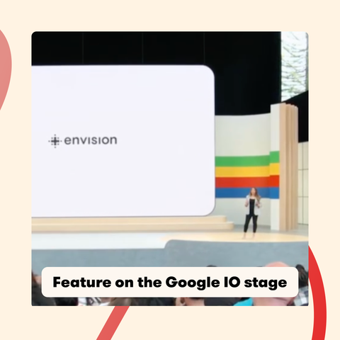 A presentation at Google I/O featuring the Envision logo on a large screen. A presenter stands on stage in front of a colorful backdrop with an audience in the foreground. The text reads 'Feature on the Google IO stage.
