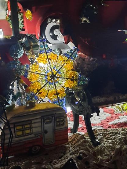 Hand beaded star using crystals, back-lit with a string light.  A miniature park bench is a perch for a metal cardinal oenament.  A cozy camper ornamental is tucked into the intimate scene. Crochet doilies mimic texture as if sand on a beach.