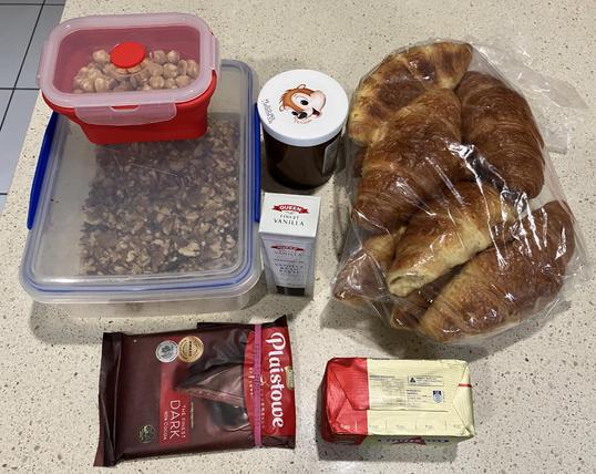 A collection of ingredients for Bread & Butter Pudding - hazelnuts, walnuts, hazelnut spread, vanilla past, cooking chocolate, and croissants.