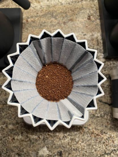 An overhead shot of an Origami coffee drippre, with ground coffee beans sitting in it.