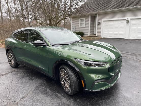 A green electric SUV parked in a driveway, with a house and trees in the background. The vehicle features a sleek design and stylish alloy wheels.