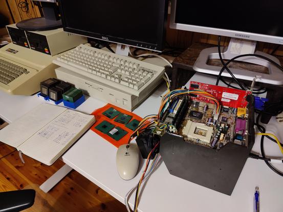 Desk with bunch of computers, a motherboard on a custom 3d-printed jig and lots of CPUs.