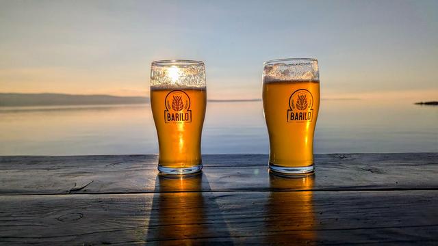 2 Gläser Bier ein lokalen Brauerei auf einer Holztheke im linken Glas sieht man die untergehende Sonne, im Hintergrund das Meer und die Insel Brav.