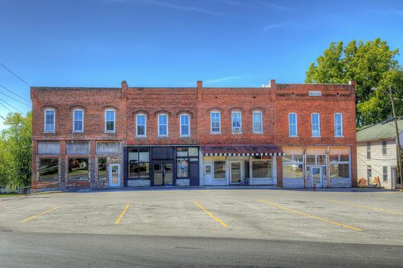 A row of historic brick buildings stands along an empty street under a clear blue sky