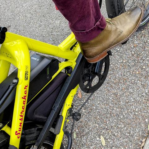 A photo of my right foot on the pedal of a 

yellow Tern HSD cargo bike with its name, Sunstreaker, in red on the seat stay

I'm wearing

Olive green boots under a deep red corduroy pantleg