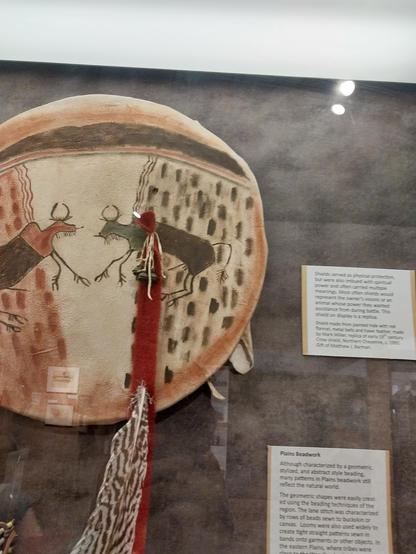Shield madle from paimed hide with red ffiammel, metal bells and hawk feather, made by Mark Miller, replica of early 19 century #Crowshield, Northem #Cheyenne, c. 1980
