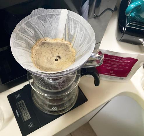 v60 coffee brew in progress, with a bag of Decaf Project beans in the background