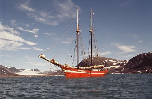 Das Foto zeigt ein Segelschiff vor der Küstenlinie Spitzbergens, an der manlinks  einen zurückgezogenen Gletscher erkennen kann, der nicht mehr ins Meer ragt.  Foto © Wolfgang Opel