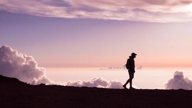 Silhouette of person walking on mountain ridge.