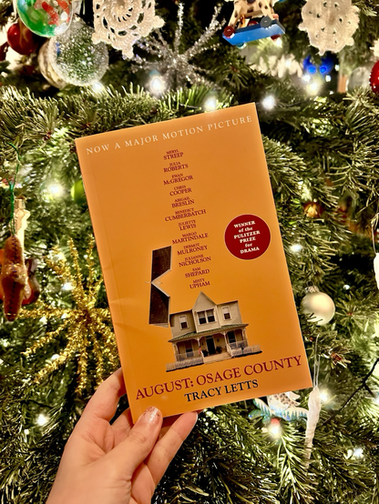 Book cover of the play August: Osage County by Tracy Letts held in front of a Christmas tree.