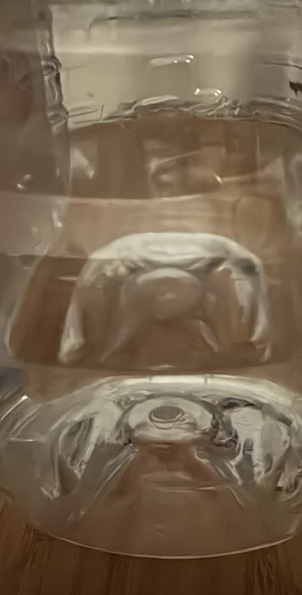 Looking into the side of a plastic cordial bottle partly filled with water, both reflections and refractions turn the water, plastic, light and wooden table beyond into an abstract of light and colour.