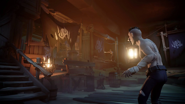 A pirate wearing cloth hand-wraps and dark trousers holding a lamp while exploring a dilapidated room. The room is scattered with barrels, planks, a lit ironwork brazier and pieces of various mechanism as well as several flags dyed with a skull-impaled-on-spikes motif. In the background is another pirate, similarly dressed, carefully examining a far corner of the room.