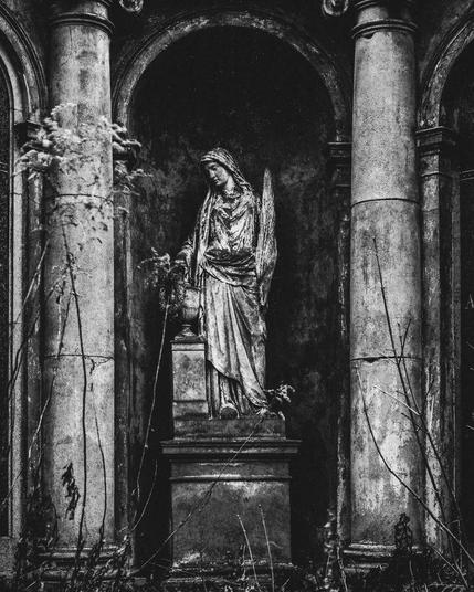 A statue of a woman, possibly an angel or religious figure, with wings and flowing robes. The statue appears weathered and aged, with signs of wear and tear.