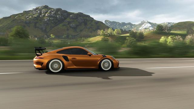 oranger Porsche GT3 schnell fahrend auf Straße vor Bergen