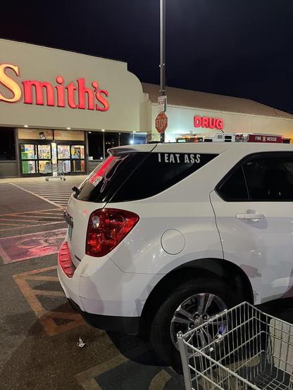 Car with decal saying “I eat ass” in the parking lot of a Smith’s grocery store at night.