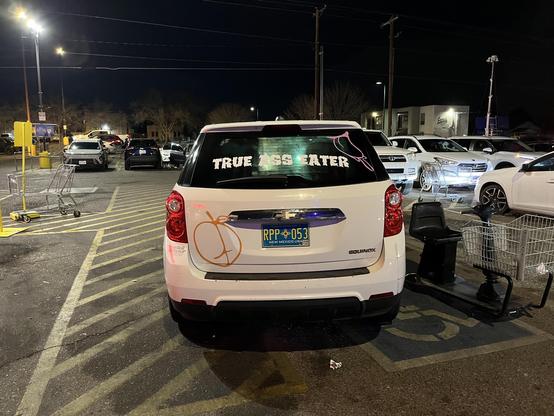 Car with the decals saying “true ass eater” and a peach that looks like a butt in the parking lot of a Smith’s grocery store at night.