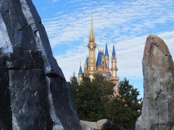 Photo of Cinderella Castle at Walt Disney World's Magic Kingdom with wispy clouds behind it and rock formations in the foreground