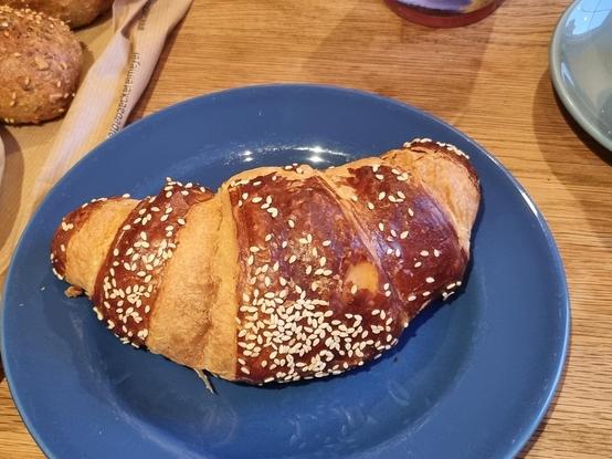 Ein Laugencroissant mit Sesam auf einem blauen Teller