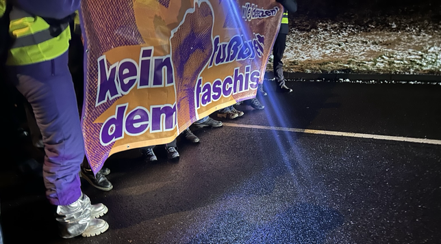 Zwei Personen halten auf einer dunklen Straße ein Transpi auf dem steht „kein fußbreit dem faschismus