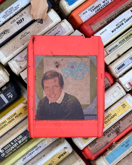 Color photo of an Andy Williams 8-track tape resting on rows of other 8-track tapes featuring musical artists from the 1970’s like Barry Manilow, Tammy Wynette, and Jose Feliciano.