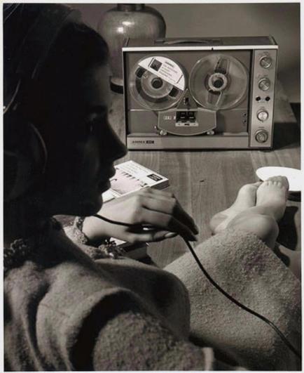 Woman in headphones pictured in silhouette listening to a vintage reel-to-reel tape recorder.