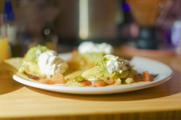 a trio of small breakfast tacos. They're topped with bacon, scrambled eggs, pico de gallo, guacamole, sour cream, and malt vinegar.