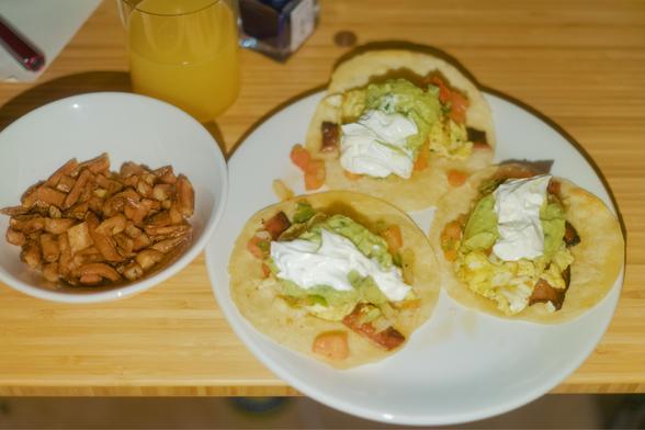 Breakfast tacos, a bowl of hash browns, and a glass of mango/peach/orange juice.
