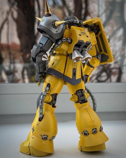 A detailed model of a yellow robotic character with spikes, featuring mechanical arms and a futuristic design. The figure is positioned from the back, showcasing its unique features and coloring against a blurred background.