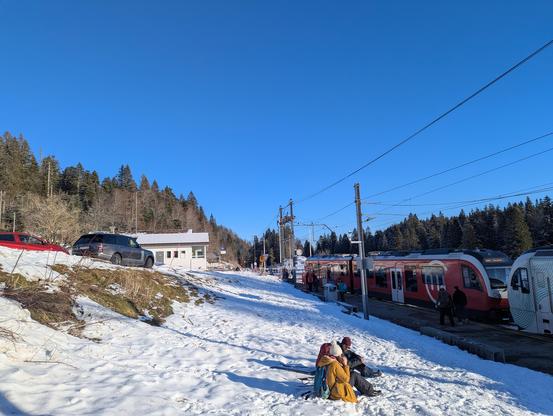 Autre vue sur le train à La Givrine, des randonneurs assis dans la neige boivent de leur thermos.
