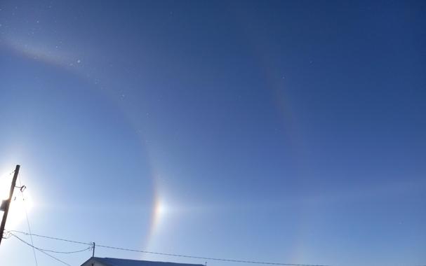 Another view with the Sun blocked by the telephone pole, this time with more focus toward the right of the sun, where there's a thin white line that travels away from the sun dog (bright rainbow spot at the same elevation as the sun), at the same elevation as the sun.