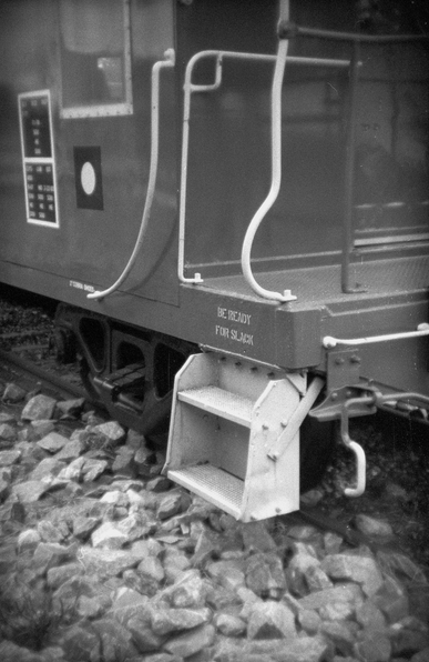 Closeup photograph of a train caboose with a sign that says "Be Ready for Slack" above a step up onto the caboose platform. 