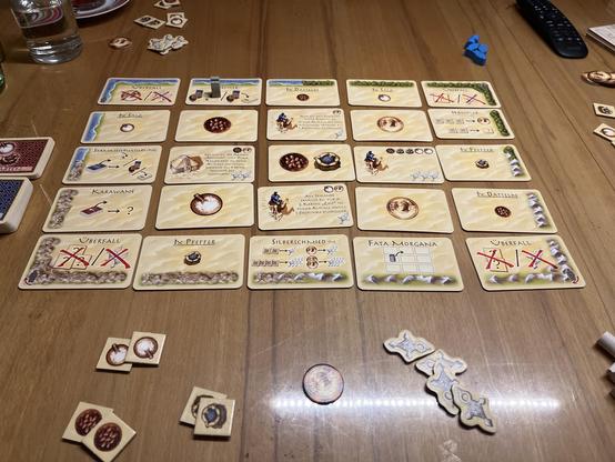 Das Spiel Targi. 5x5 Karten in einem Raster ausgelegt. Am Rand verschiedene Chips und zwei Nachziehstapel