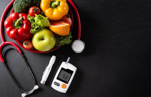 Bowl of vegetables surrounded by stethoscope and diabetes monitor. 