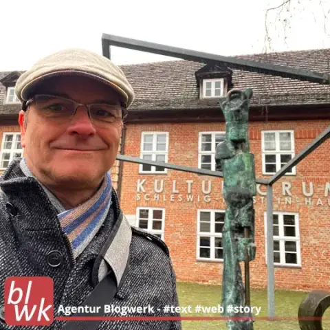 Oliver Hübner vor dem Kulturforum Schleswig-Holstein-Haus in Schwerin, Backsteingebäude, Skulptur, Mann mit Kappe