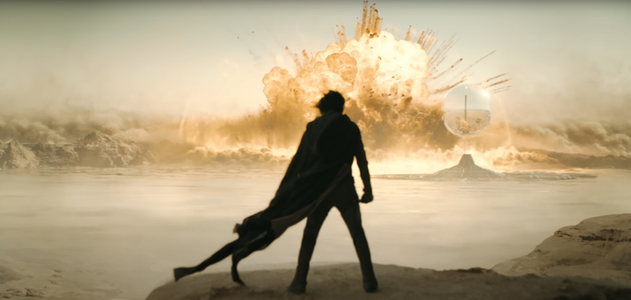 Shot from Dune: Part Two, showing Paul Atreides at the beginning of the climatic final battle with an explosion and the Emperor's ship in the background