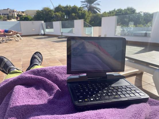 A Canarian hotel patio with sunbeds and palms in the distance on a sunny day. On the first plane, me on a sunbed, with a GPD Micro PC running Emacs and displaying some Clojure code