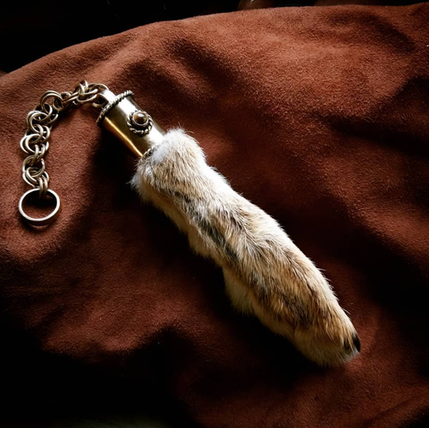 A jeweled rabbit's foot with a chunky chain rests on a piece of leather. 