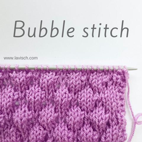 A swatch in lilac yarn on a gray knitting needle, showing the bubble stitch.