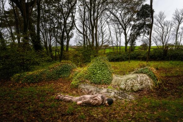 Planking im Wald neben einer liegenden Frauenskulptur