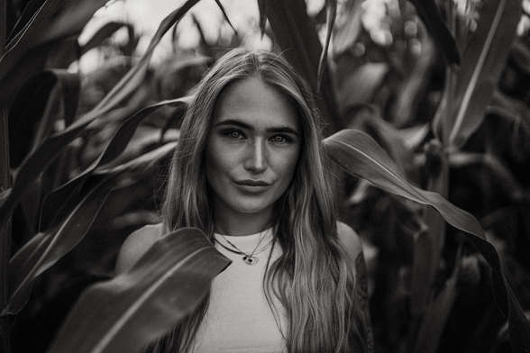 Black-and-white portrait photo of a girl in a cornfield.