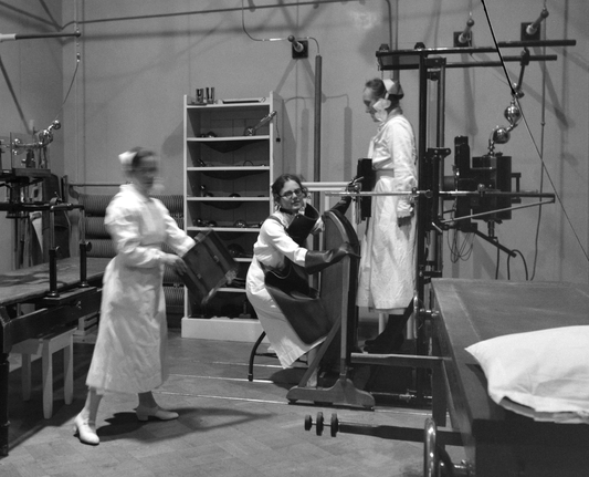 Kuva 1900-luvun ensimmäiseltä vuosikymmeneltä. 

Sairaalan henkilökuntaa tutkimushuoneessa, Pietarinkatu 24:ssä sijainneessa Eskelinin sairaalassa (1905-1919), sittemmin Sanitas-sairaala (1919-1940). Lyijyliiviä pitävä sairaanhoitaja katsoo röntgen-kameraa kuvaa ottaessaan ilman kasvosuojausta.