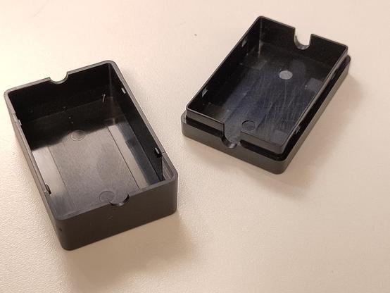 Empty small "generic" plastic case with the lid removed on a white desk. It's about 6 x 4 x 2.5 cm in size.