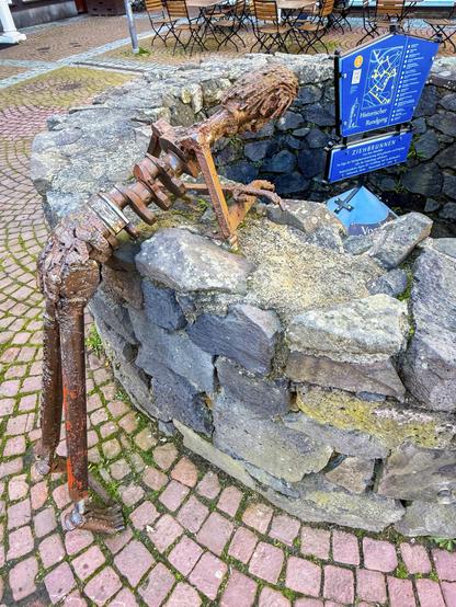 Die Skulptur "Brunnengucker" auf dem Marktplatz in Grünberg zeigt eine menschliche Figur, die sich neugierig über den Rand eines historischen Ziehbrunnens beugt.