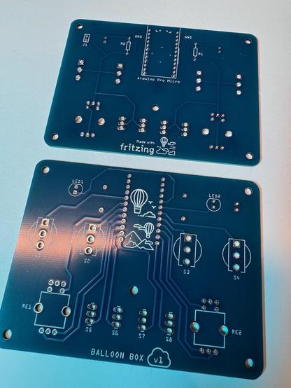 Front and back views of a pair of blue circuit boards with white lettering that outlines the positions of various components. The words Ballon Box v1 are at the bottom. 