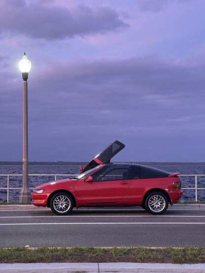 A red car in front of a lake
