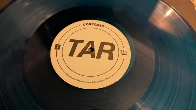 Die Vinyl auf dem Bild ist türkis durchscheinend, das Etikett beige mit brauner Schrift minimalistisches Design. 