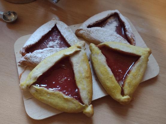 Four triangular pastries with a red filling in the centre. Two of the pastries are covered with icing sugar.