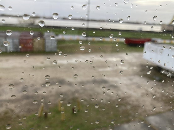 Glasscheibe mit Regentropfen - die Aufnahme ist auf die Tropfen fokussiert, aber im Hintergrund sieht man unscharf einen grünen Deich und den Mississippi