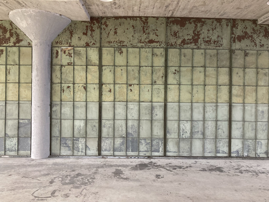 Blick auf eine Wand, die wohl aus überstrichenen Fensterscheiben besteht - sie hat jetzt eine grau-grüne Farbe.