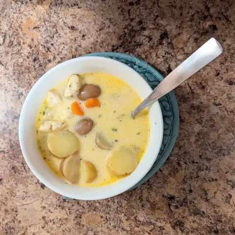 Image shows a white bowl filled with Cajun potato and chicken soup. There's a spoon in the bowl.